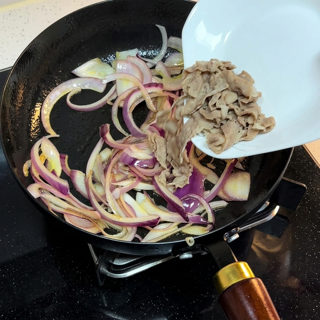Blanched beef slices being transferred from a white plate into a pan containing stir-fried onion strips.