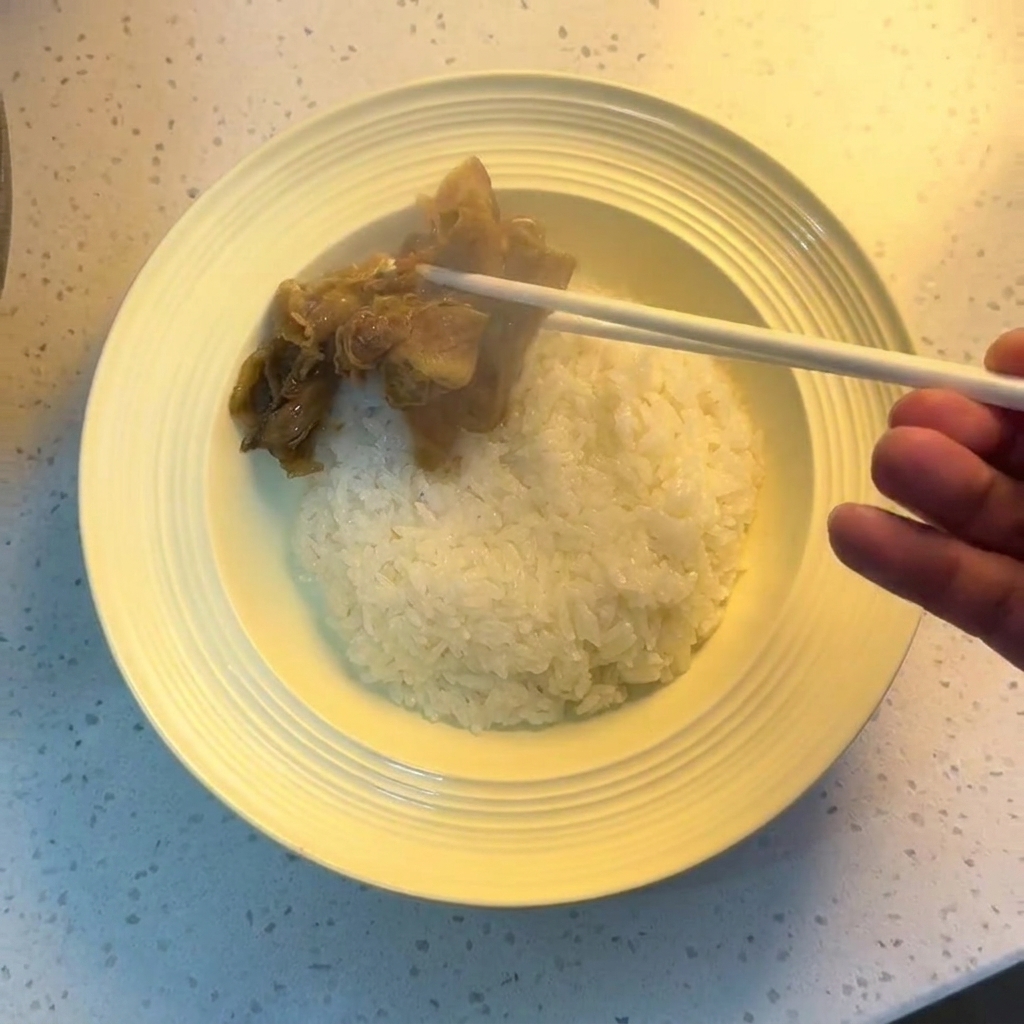 Chopsticks placing cooked beef and onions onto a bowl of white rice.