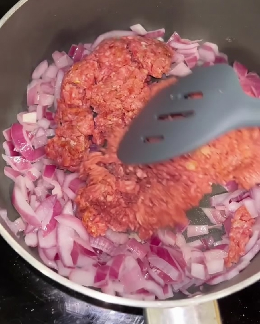 Minced beef being stir-fried with sautéed red onion in a pan.