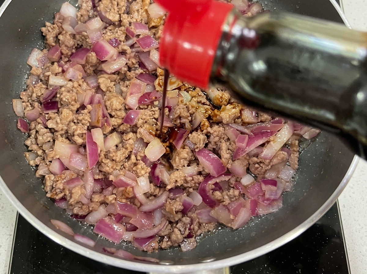 Dark soy sauce and ketchup being added to the pan of stir-fried beef and onions.