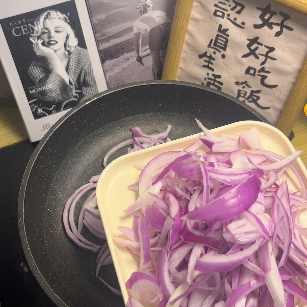 A close-up view of fresh purple onion slices being spread evenly across the surface of a non-stick pan.