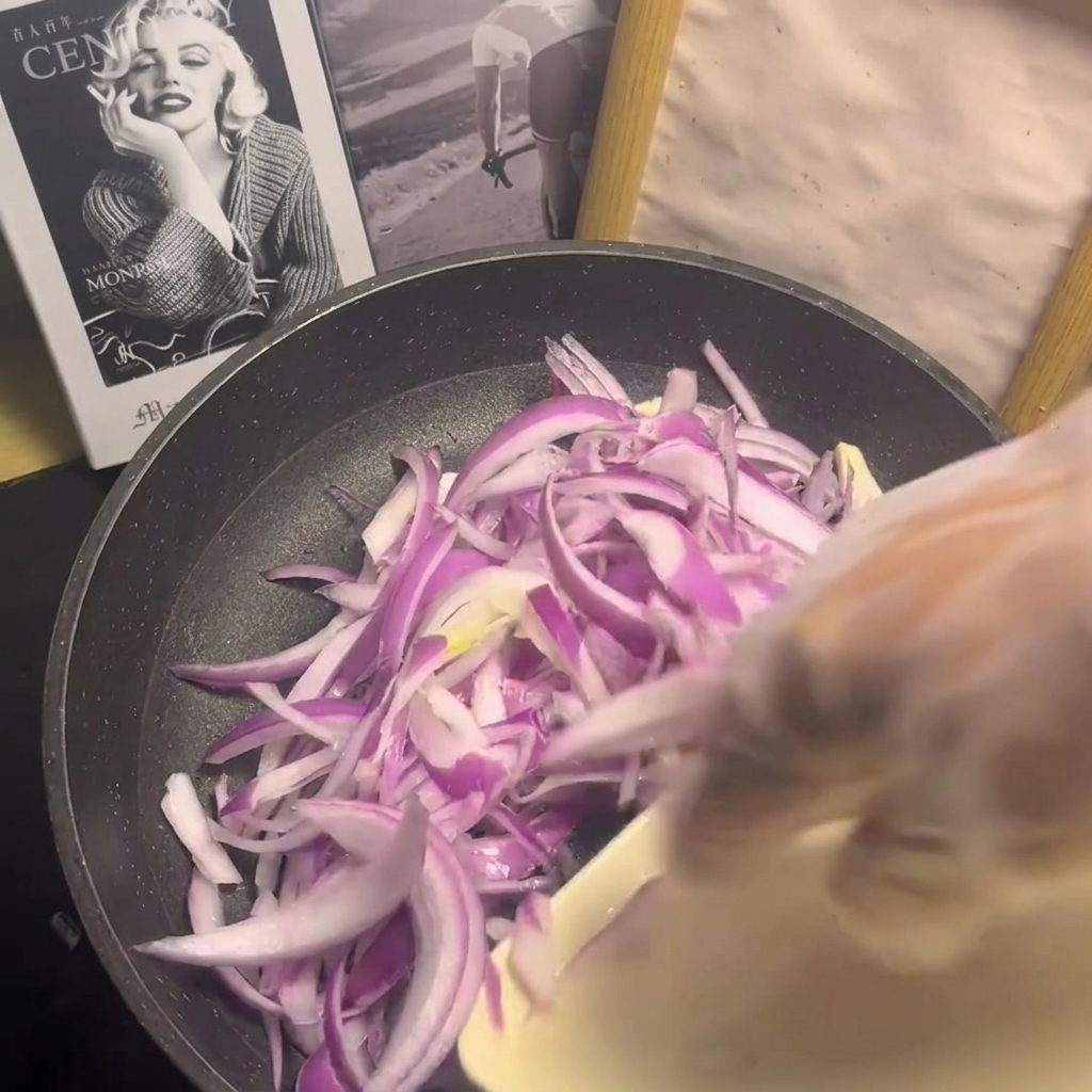 Slices of marinated beef being arranged over the bed of raw onions in the pan.