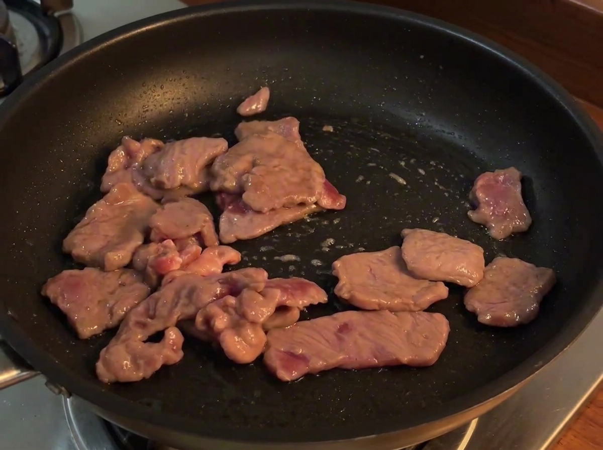 Sliced red onions added to the pan with cooked beef, being stirred together over heat.