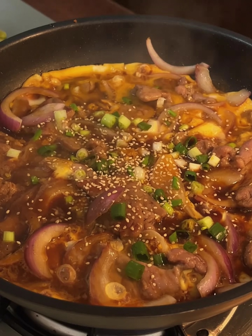 A finished beef and egg dish in a pan, topped with fresh chopped green onions and toasted sesame seeds.