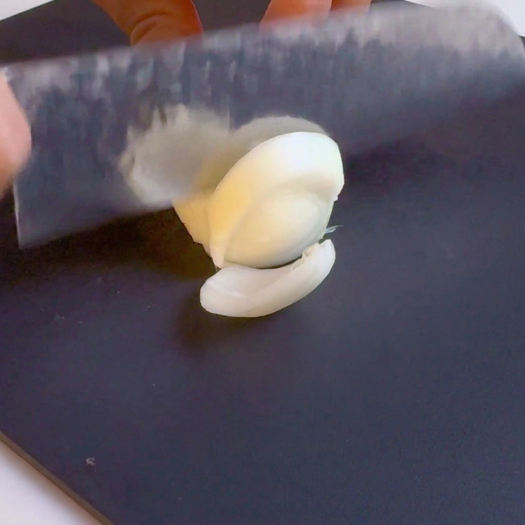 A knife slicing a white onion into strips on a black cutting board.
