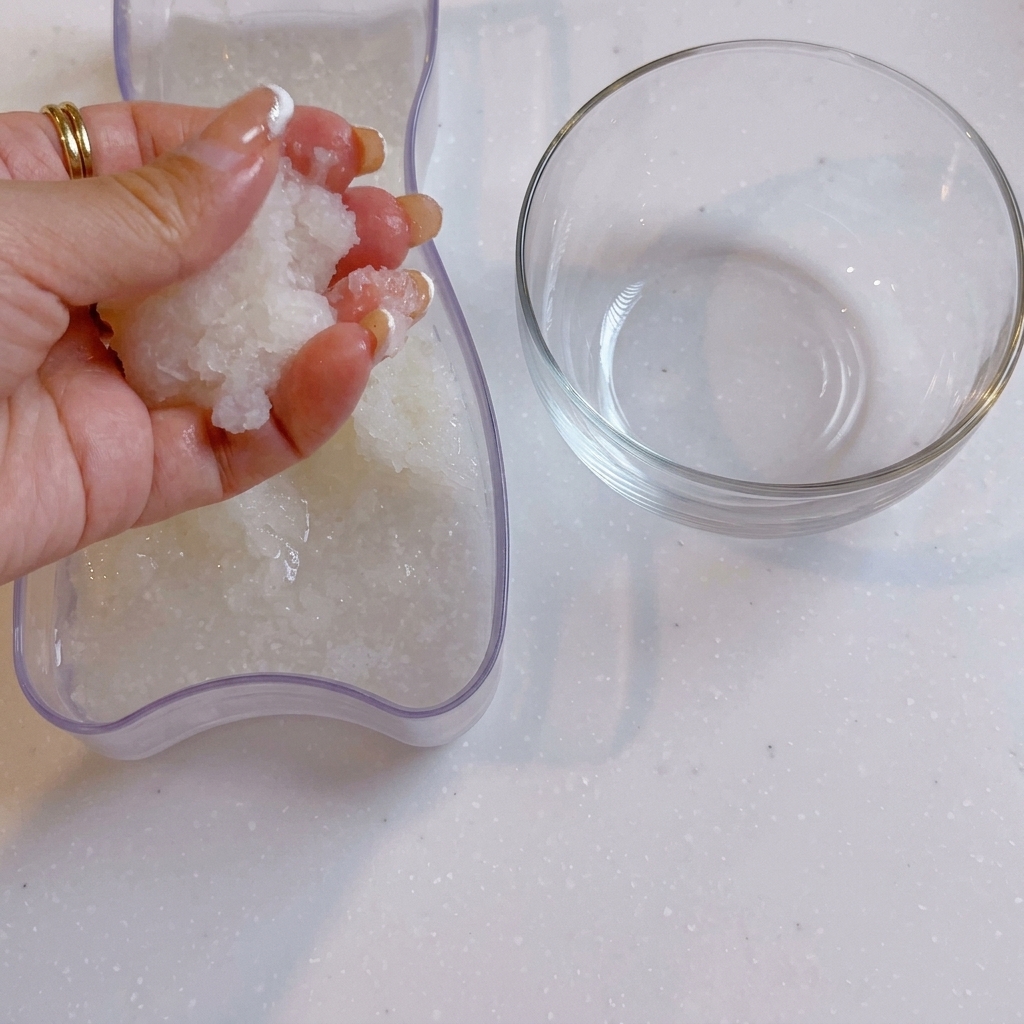 A hand squeezing water out of grated daikon radish next to a clear glass bowl.
