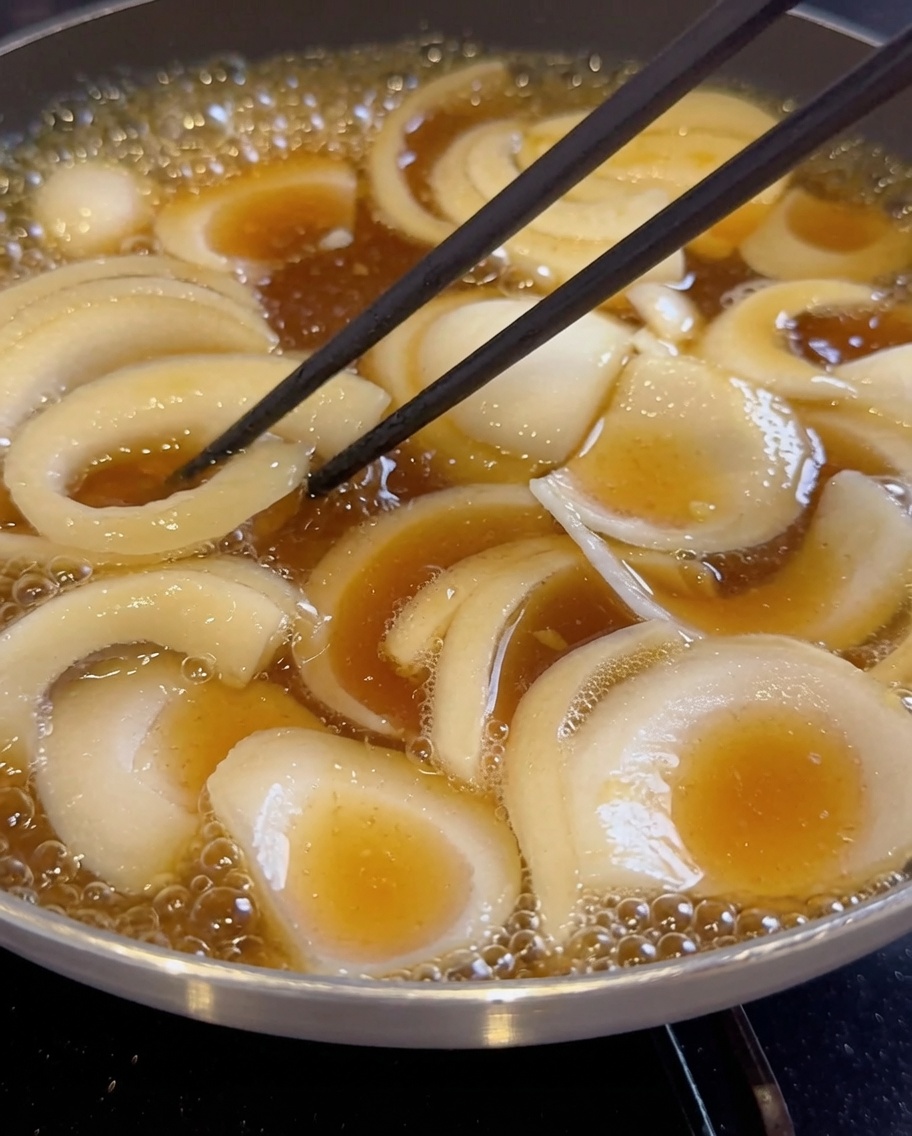Sliced onions simmering in a dark, boiling liquid in a pan.