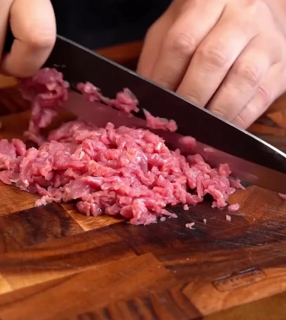 Finely minced fresh beef paste on a wooden cutting board, ready for seasoning.