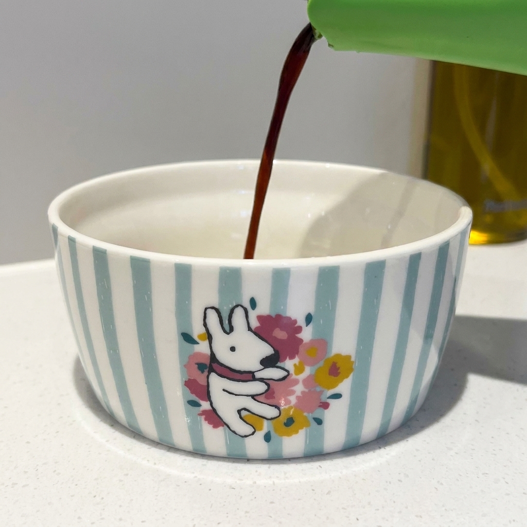 Soy sauce and other seasonings being measured into a small, decorative ceramic bowl.
