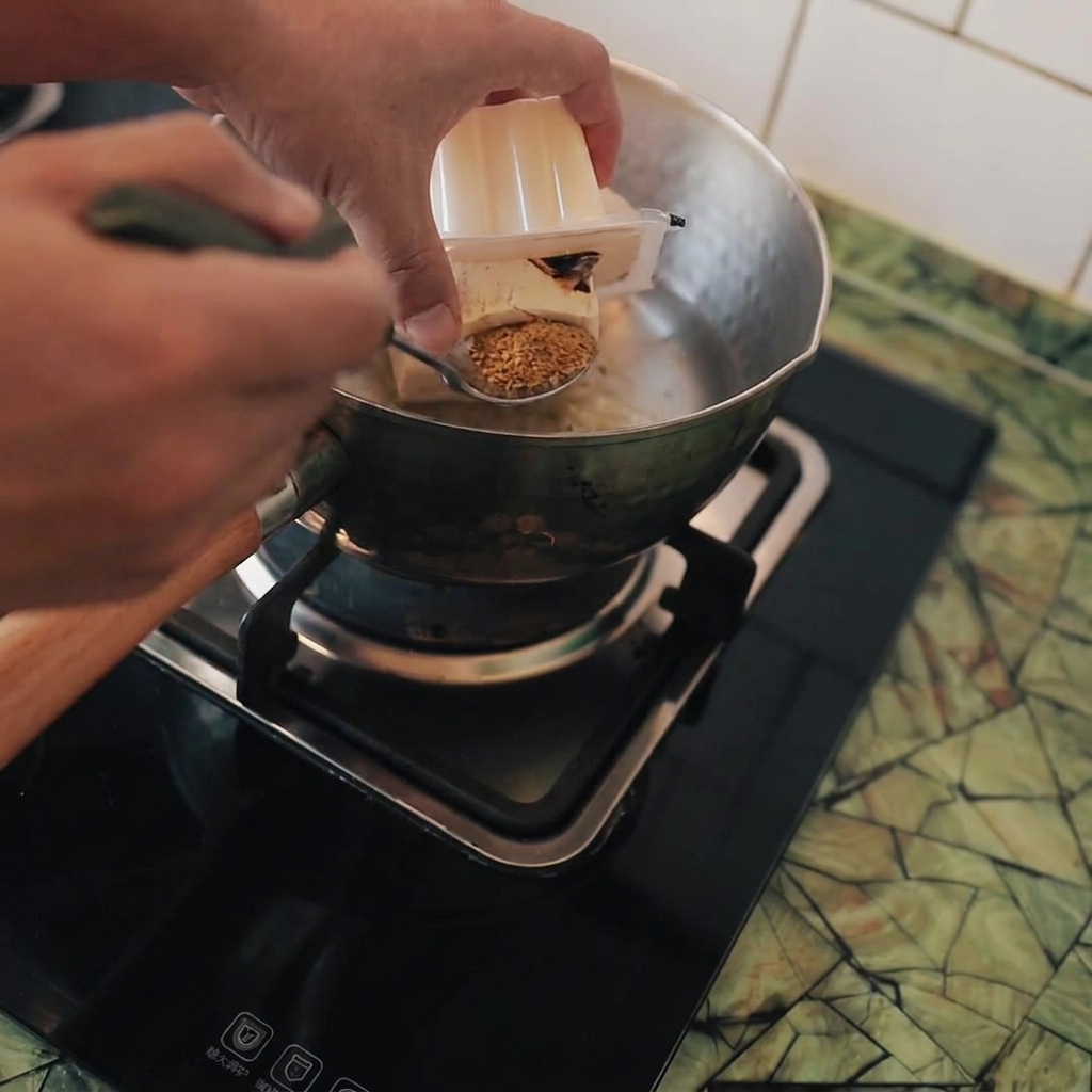 Cubed tofu being carefully added into a stainless steel pot of boiling water on a stovetop.