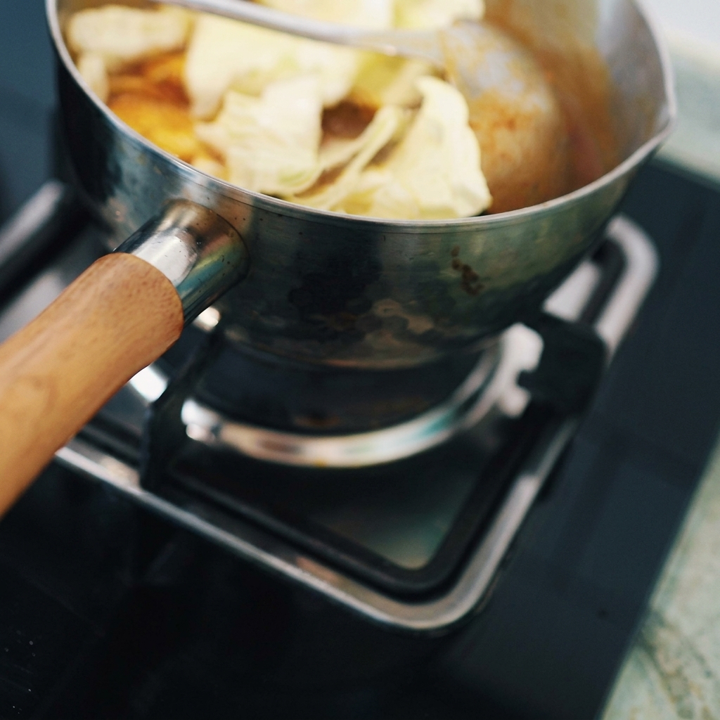 Napa cabbage pieces being stirred into the thick Japanese curry and tofu mixture in a metal pot.