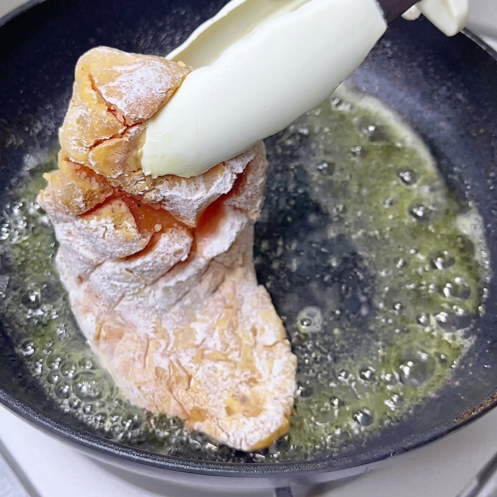 A pat of butter melting and bubbling slightly in a hot dark skillet.