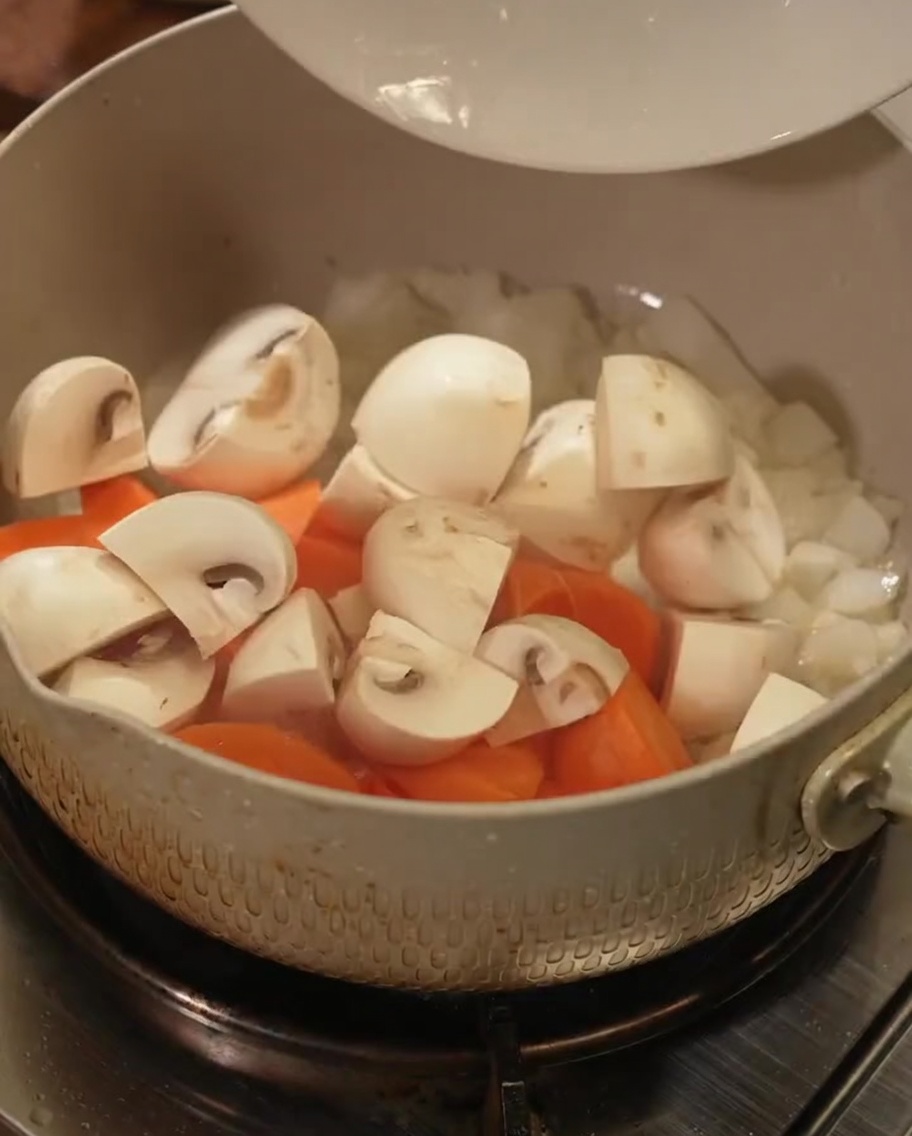 Fresh carrot chunks and mushroom slices being tossed in a cooking pot.