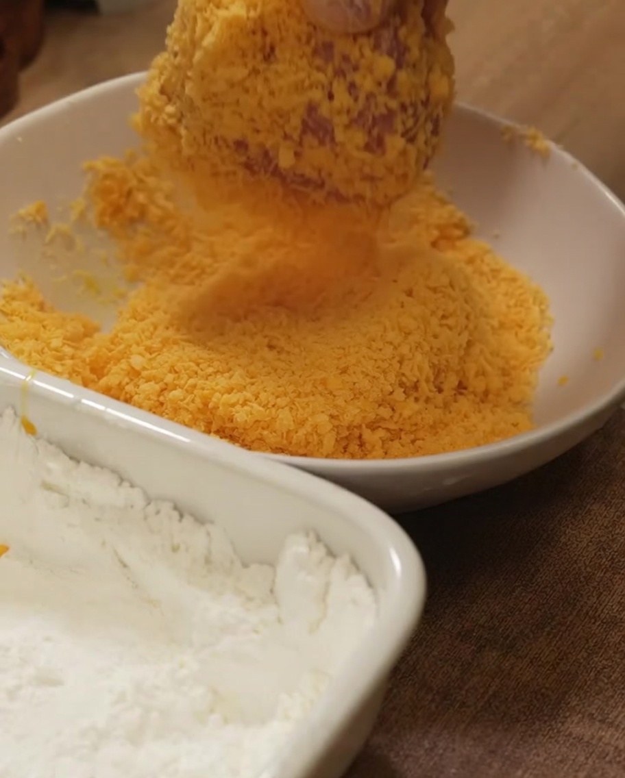 Chicken breast being pressed firmly into a bowl of golden breadcrumbs for an even coating.