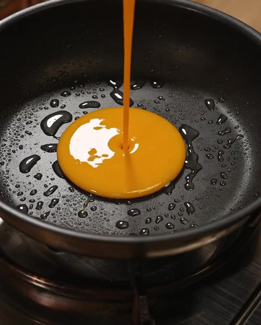Golden egg mixture being stirred in a non-stick frying pan to create light and fluffy scrambled eggs.