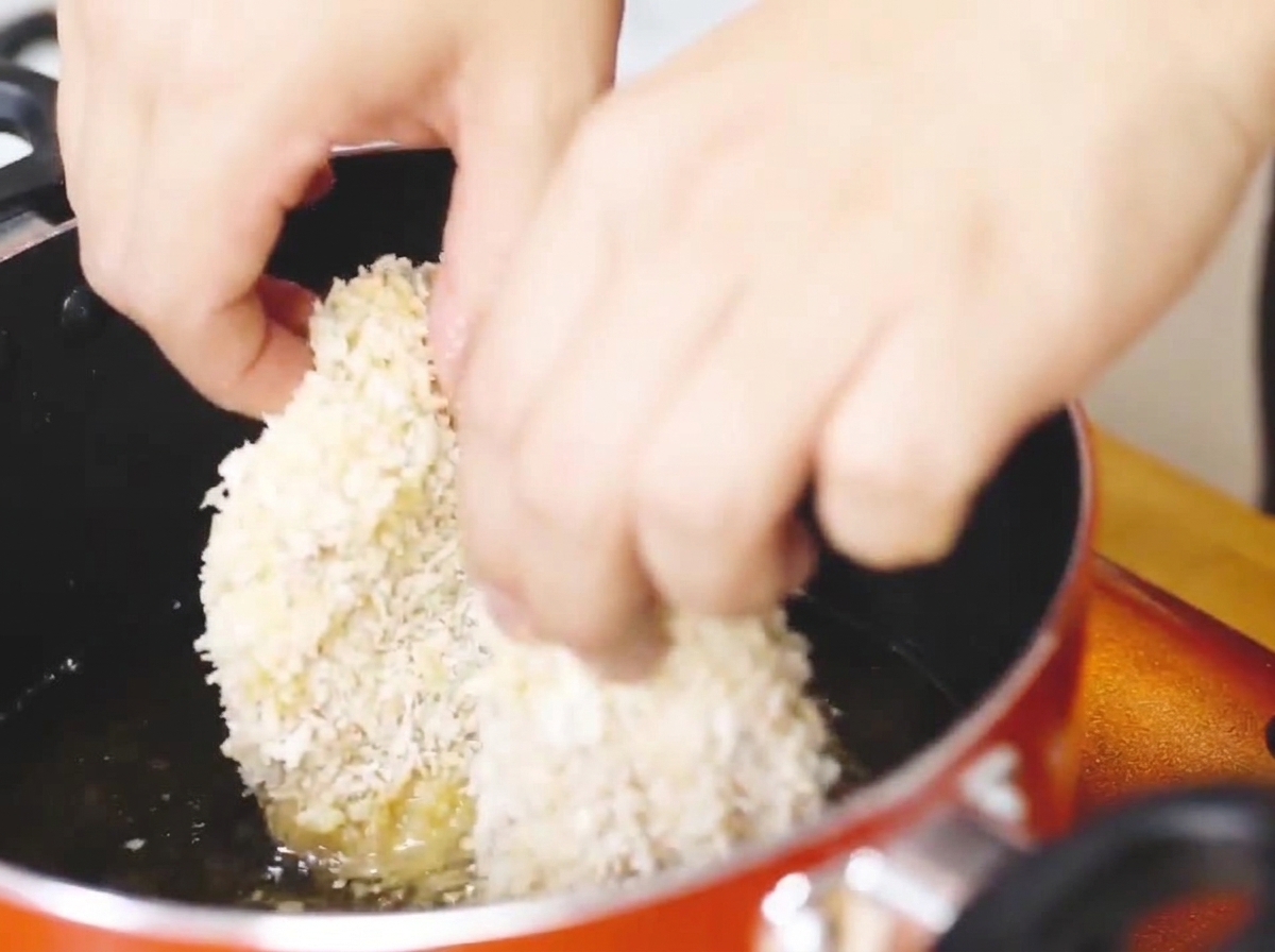 Breaded chicken cutlet frying in a pan of hot oil until golden brown.