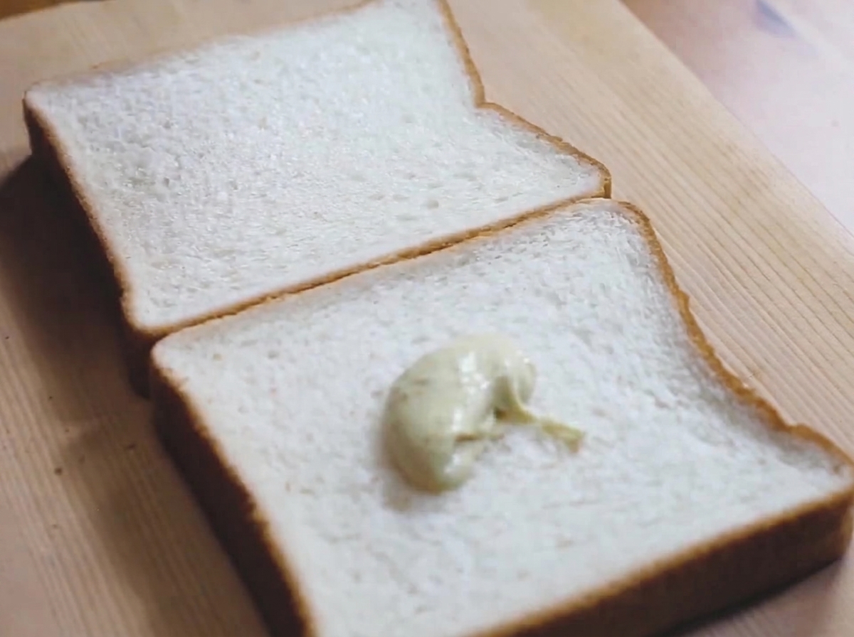 A dollop of pale green wasabi-mayonnaise sauce sitting on a slice of white bread on a wooden board.