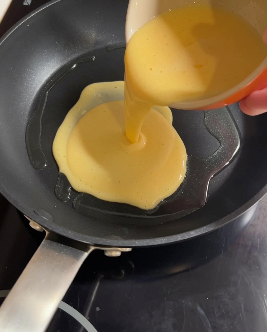 Yellow egg and milk mixture being poured into a hot frying pan, ready to be scrambled.