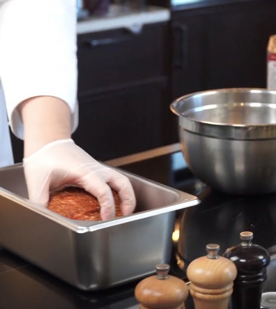 The seasoned pork being set into a rectangular stainless steel baking pan.