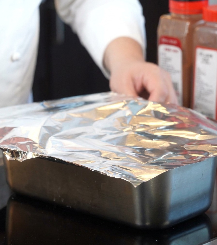 Aluminum foil being used to securely cover the top of a metal baking pan.