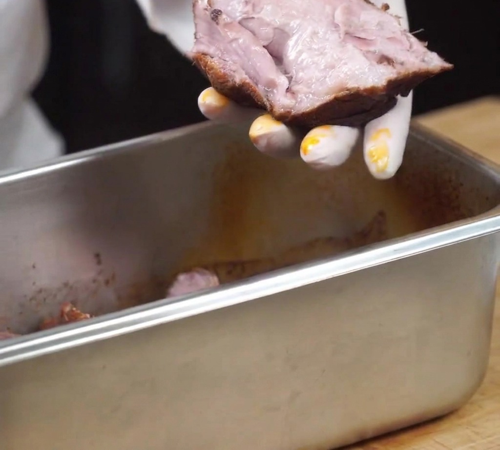 A piece of cooked, tender pork being shredded by hand.