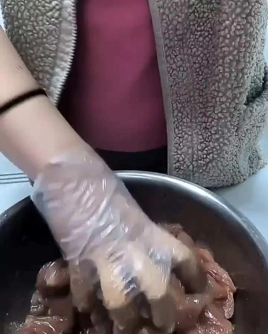 Clear cooking oil being drizzled over seasoned raw pork pieces in a metal bowl.