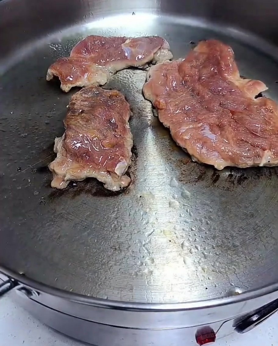 Marinated pork chops searing in a hot frying pan with visible browning on the surface.