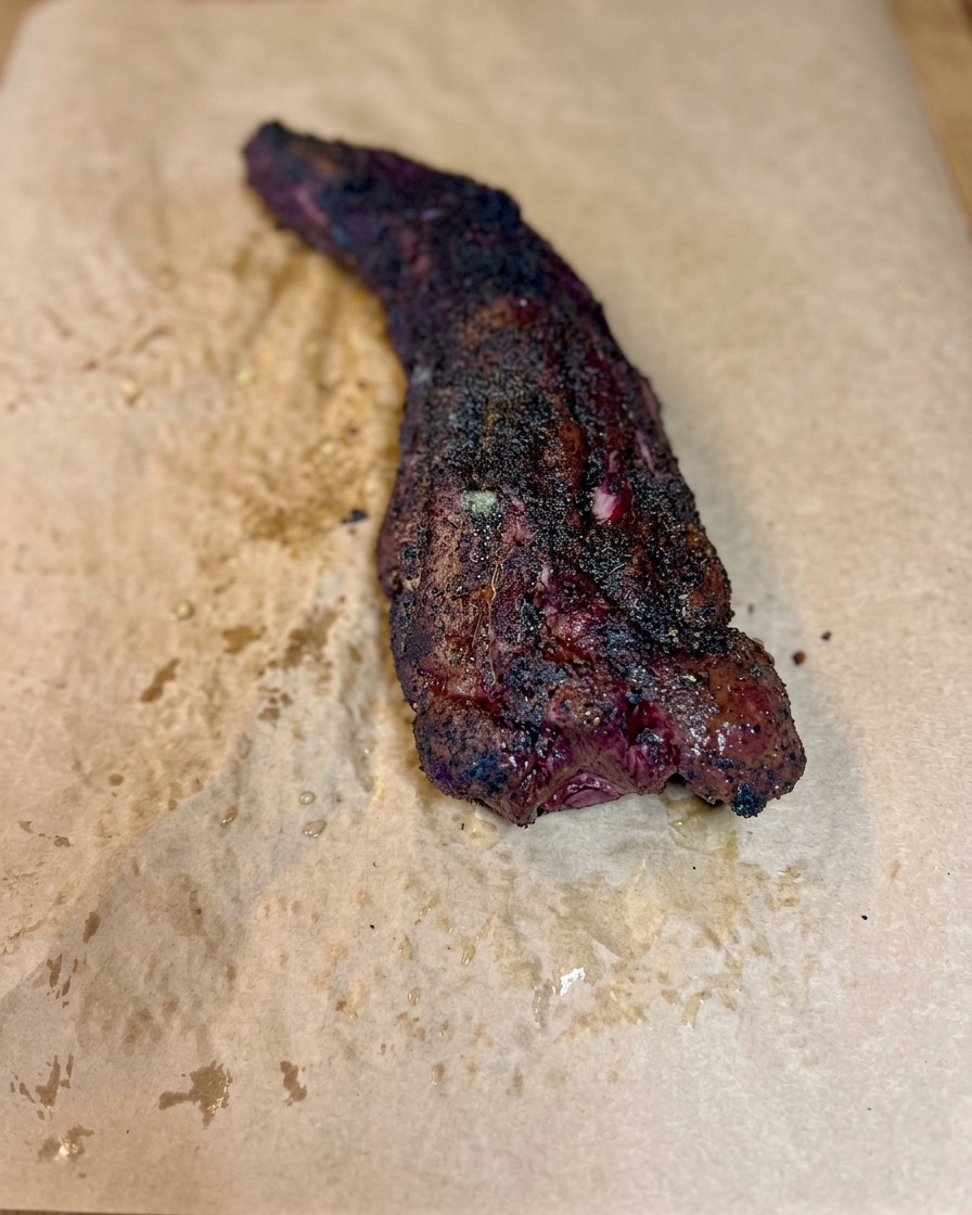 A smoked beef rib being rolled tightly within butcher paper to form a complete package.