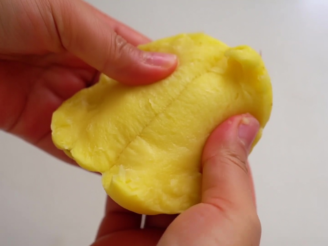 Hands pulling a peeled potato into two rough halves.