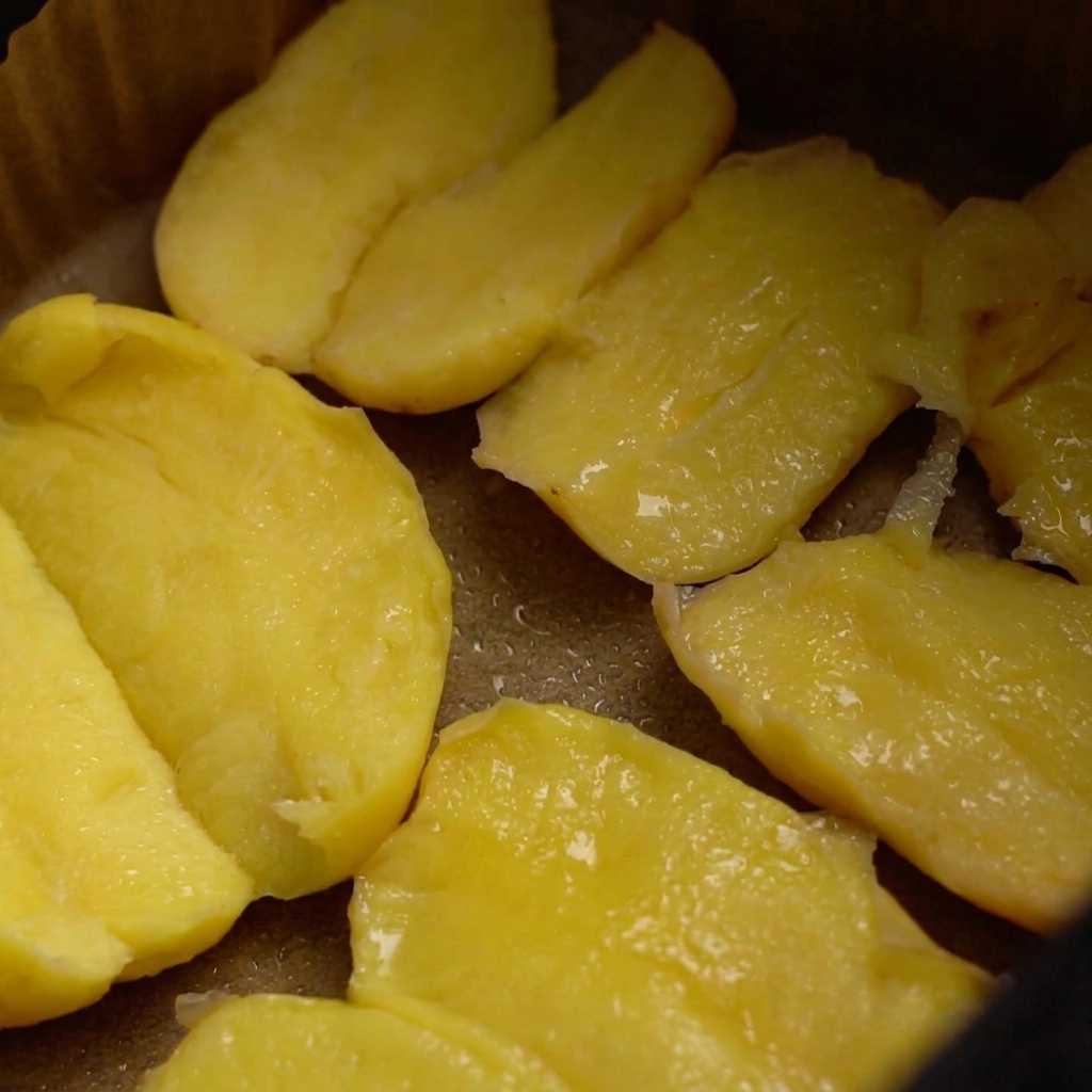 Potatoes in an air fryer basket coated in oil, being seasoned with coarse salt and a scattering of sesame seeds.
