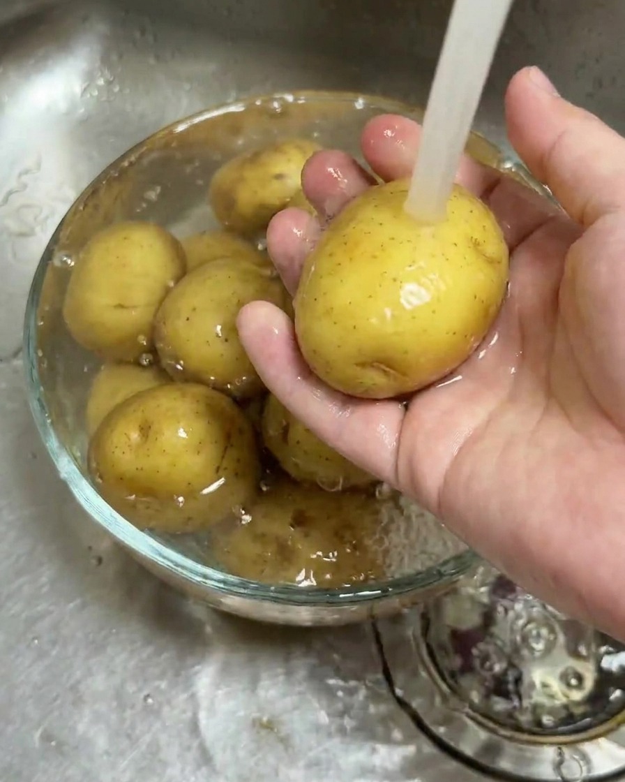 Baby potatoes being cleaned in a glass bowl under a stream of running water.