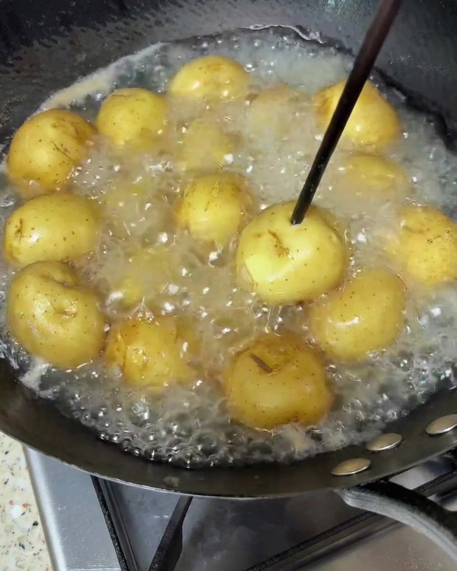 Baby potatoes simmering in boiling water, with a wooden chopstick being used to check if they are tender.
