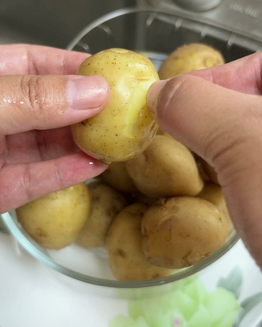 Close-up of hands removing the thin skin from a boiled baby potato.