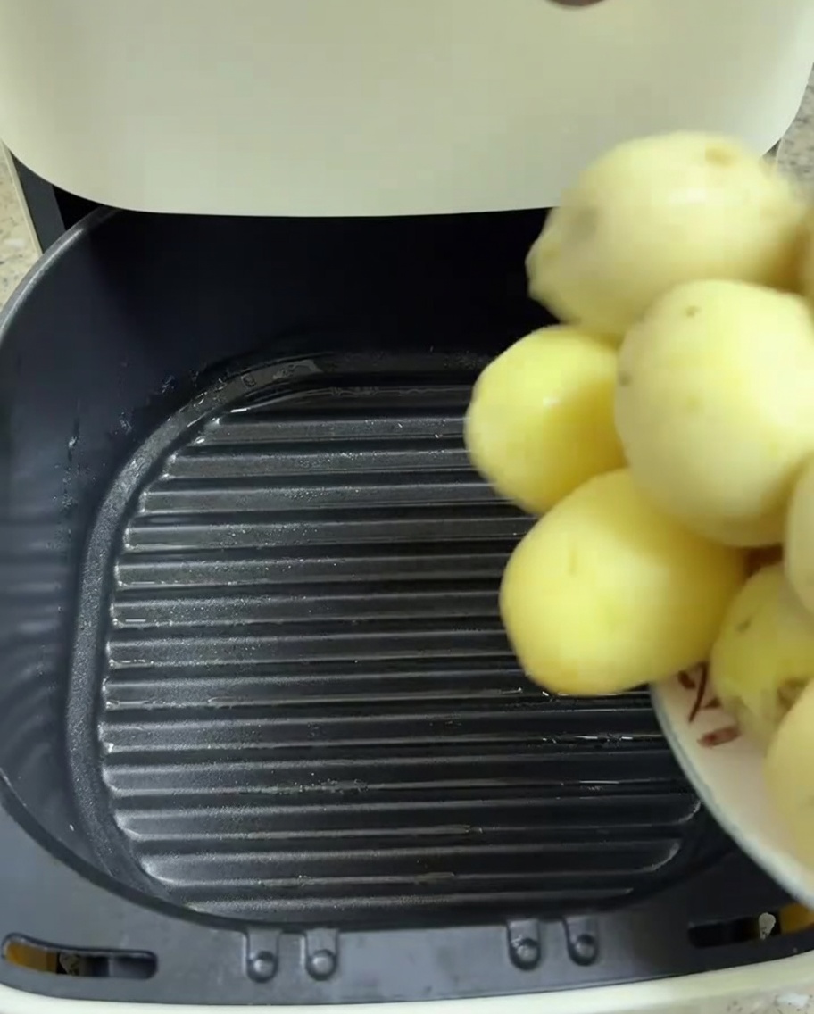 Peeled baby potatoes being transferred into the air fryer basket.