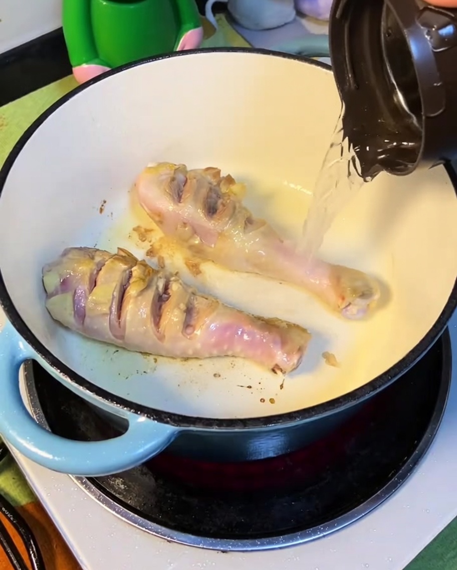 Boiling water being poured into the pot with seared chicken.
