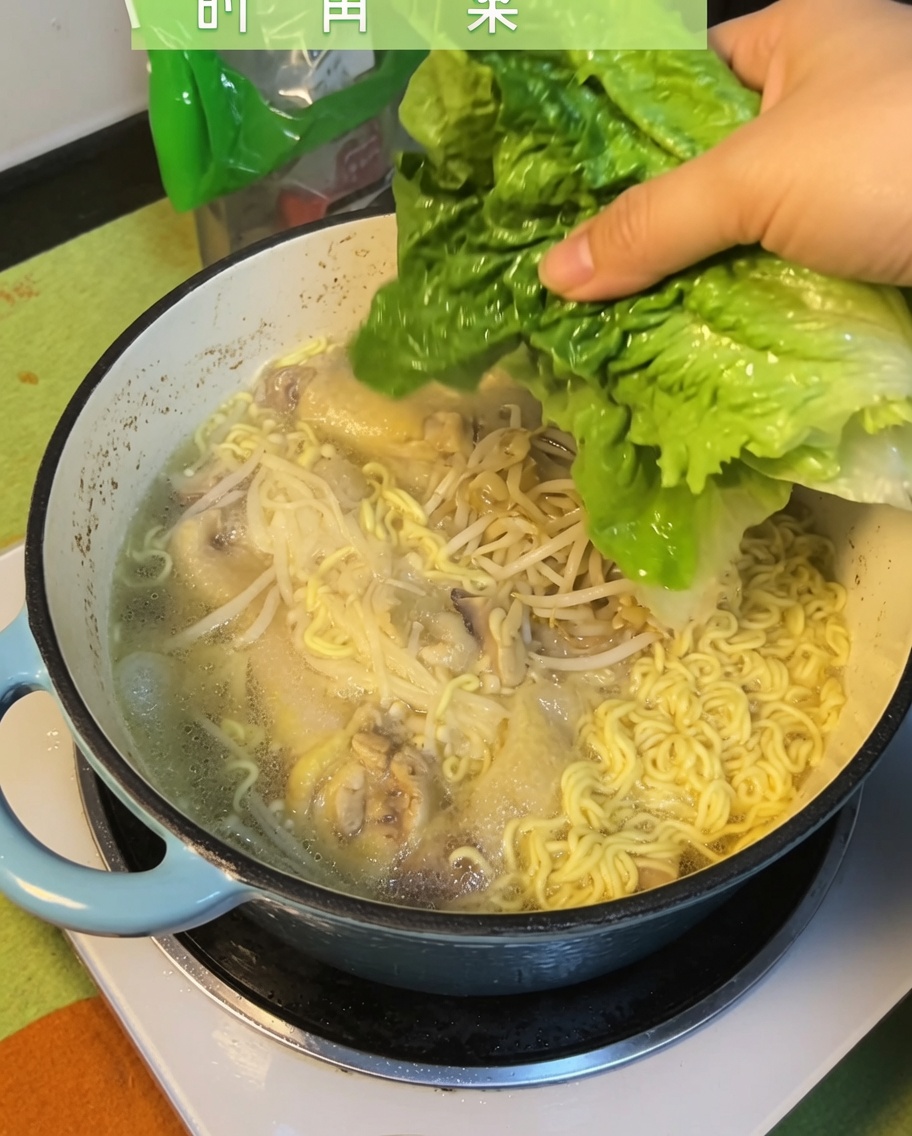 Fresh green bok choy leaves being added to the finished chicken noodle soup.