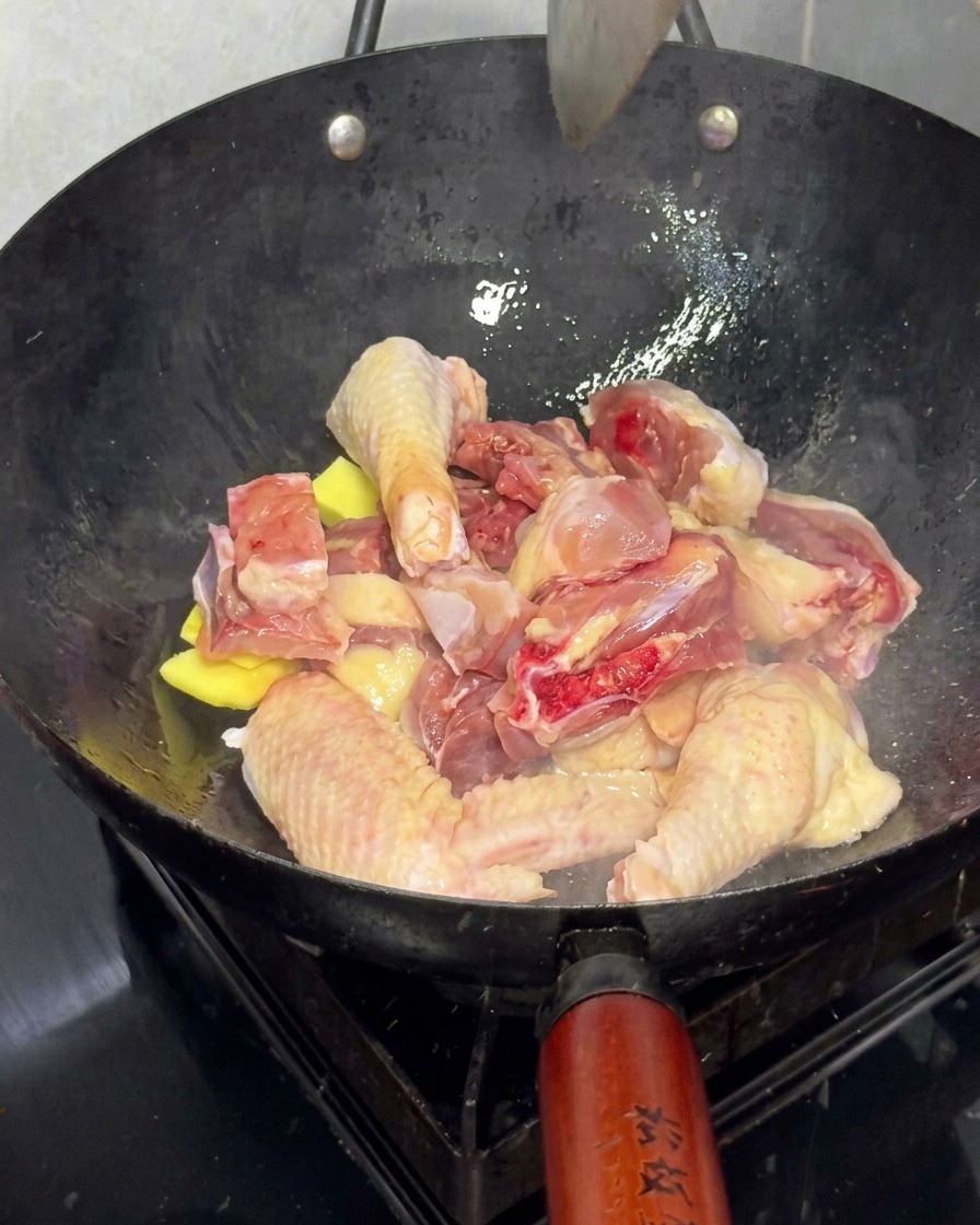 Fresh chicken pieces being stir-fried with ginger slices in a large wok.