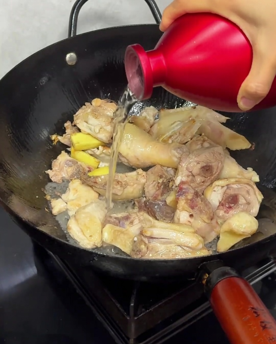 Rice wine being poured over chicken pieces in a wok during the stir-frying process.