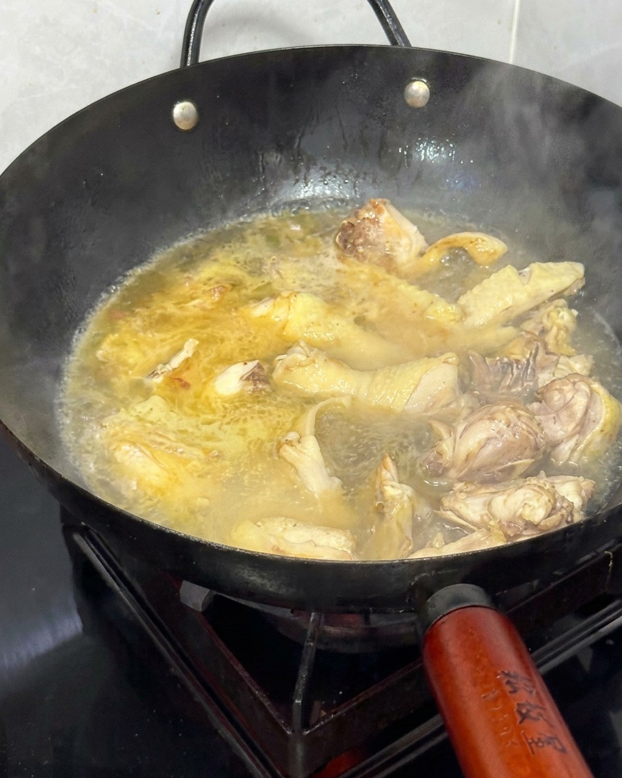 Hot water being added to a wok filled with stir-fried chicken and ginger.