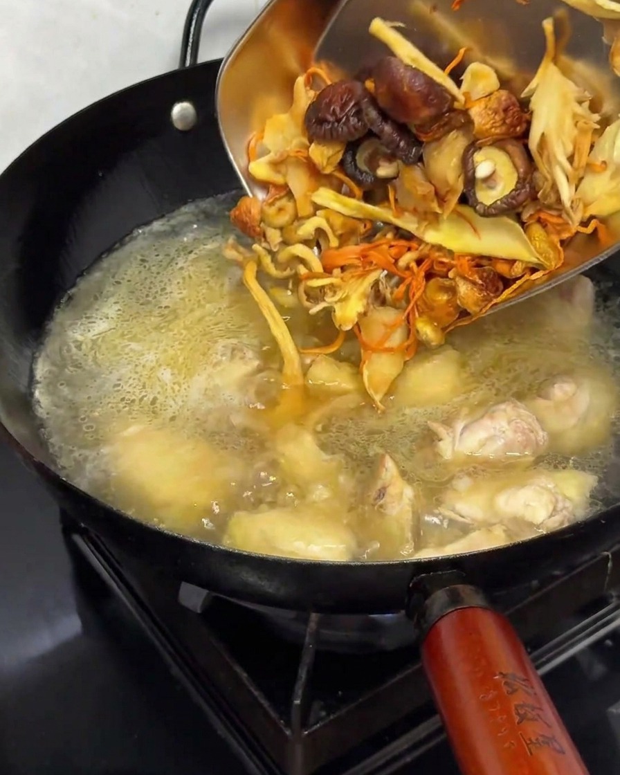 Rehydrated dried mushrooms being added into a pot with chicken and broth.