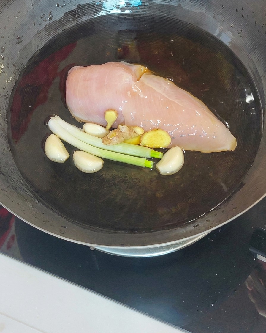 Cooked chicken breast being lifted from a wok using a slotted spoon and chopsticks.