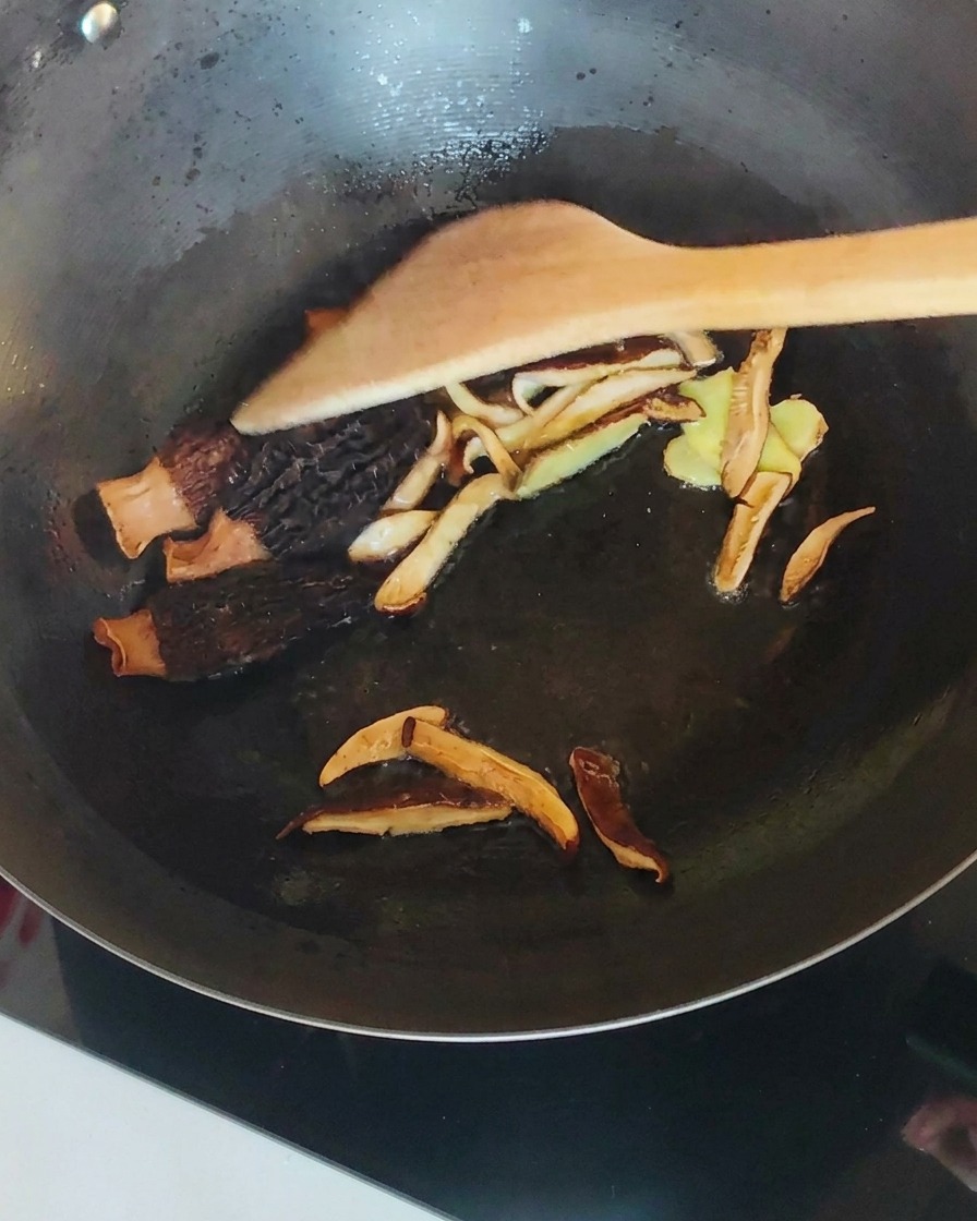 Shredded chicken mixed with mushrooms and ginger in a wok.