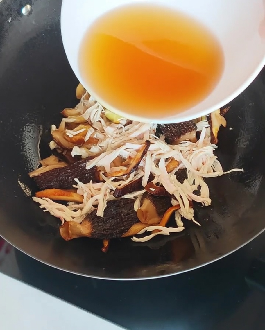 A clear, amber-colored mushroom soaking liquid being poured into a wok containing chicken and mushrooms.