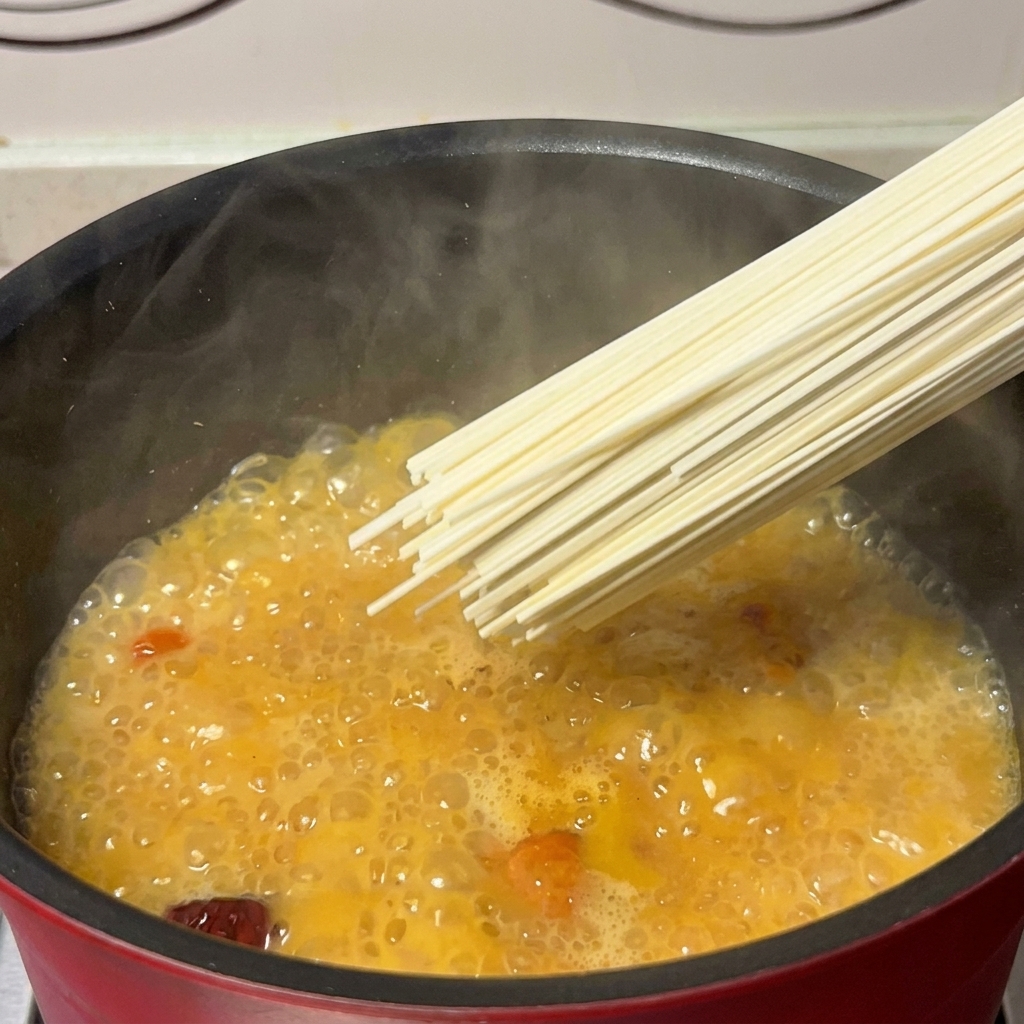 A handful of dry noodles being lowered into a pot of golden, simmering chicken and mushroom broth.