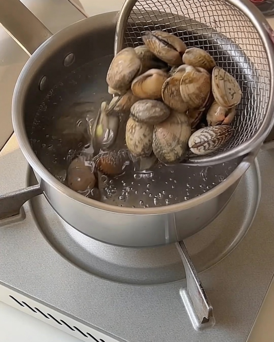 Clams in a mesh strainer being lifted out of a pot of boiling water.