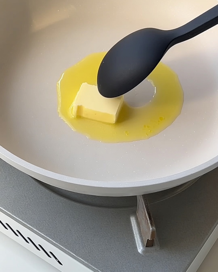 A smooth white sauce thickening in a pan, being stirred with a spoon.
