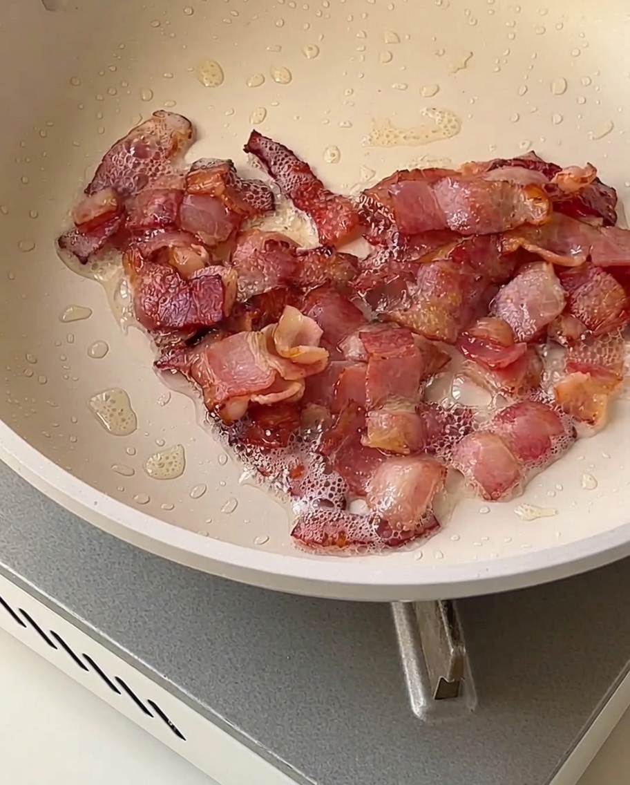 Onion, celery, and potato cubes frying in a pan with pieces of golden-brown crispy bacon.
