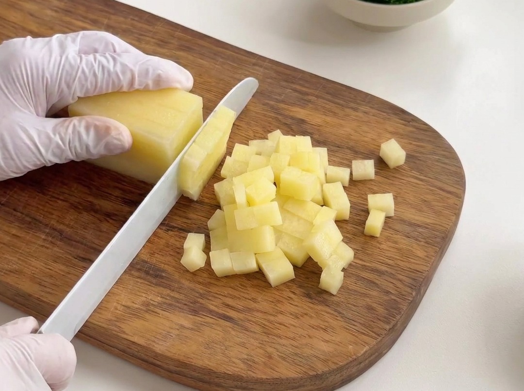 Peeled potatoes being cut into small, consistent cubes on a wooden cutting board.