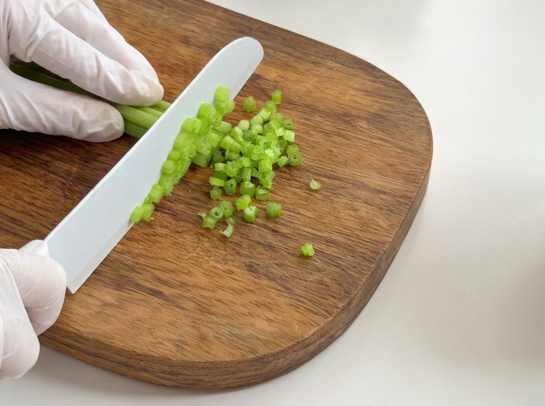 Fresh celery stalks being chopped into small pieces on a wooden cutting board.