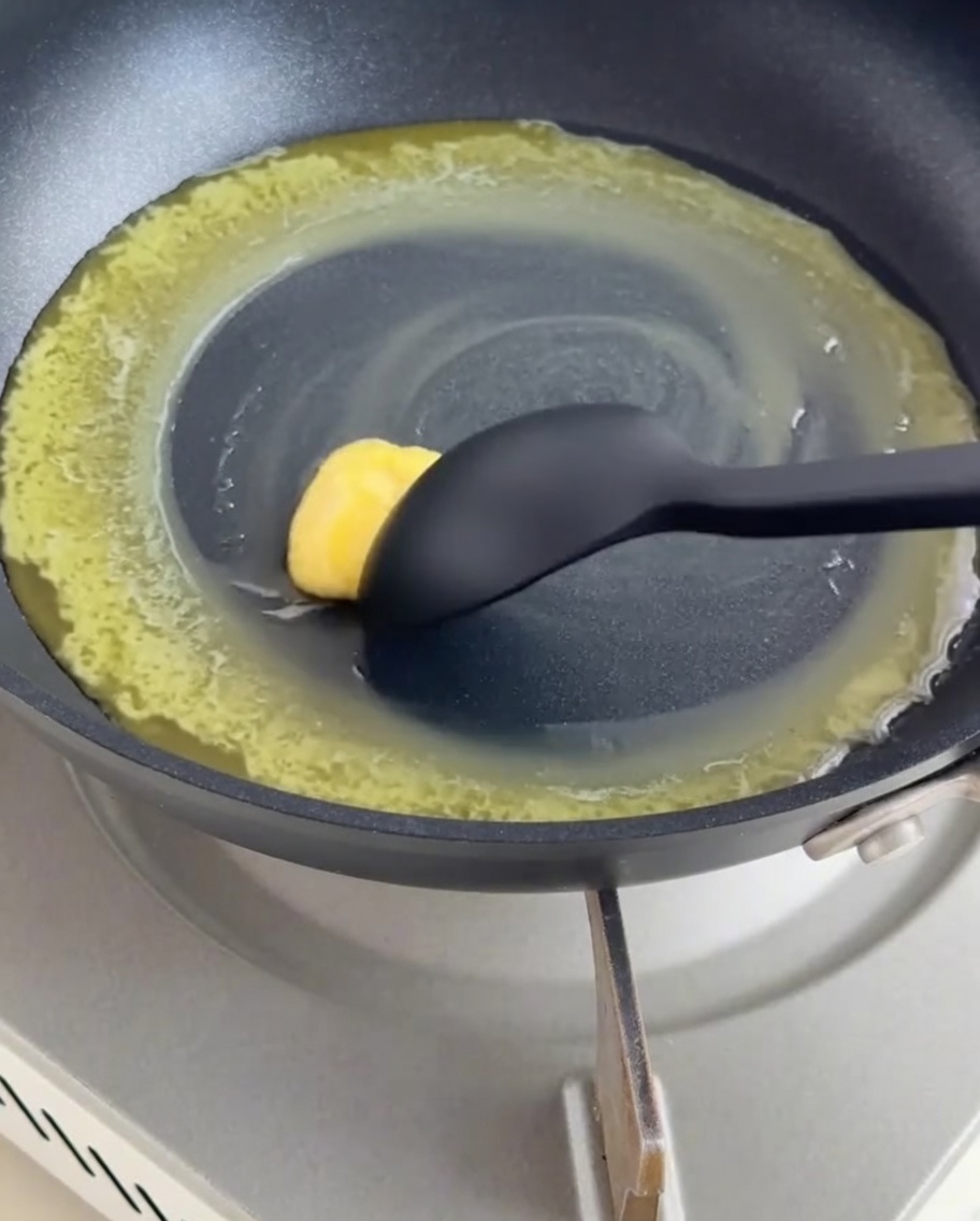 A dark non-stick pan containing melted butter and flour being mixed into a roux with a black silicone spatula.